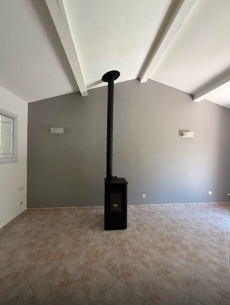 Même séjour rénové : murs repeints, cheminée supprimée, poêle noir compact avec conduit apparent