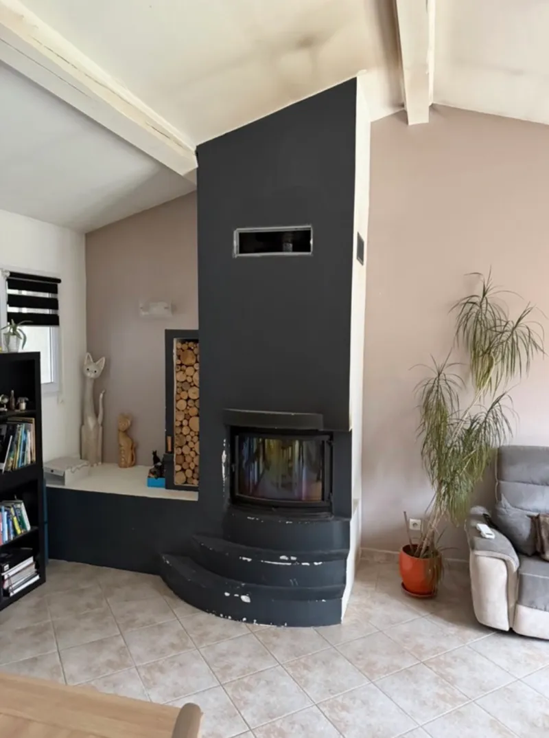 Séjour avec grande cheminée d’angle peinte en noir, avec insert et marches maçonnées, avant travaux